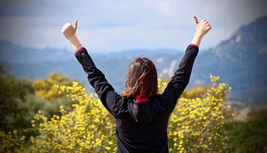 How To Walk The Fearless Path woman looking out over a valley with her two hands in the air with thumbs up