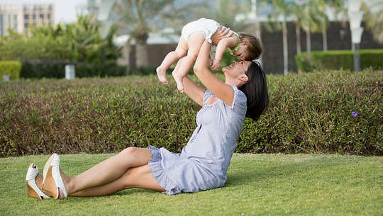 Loving Relationships and a Peaceful Soul smiling mother, sitting on the grass, holding up a child