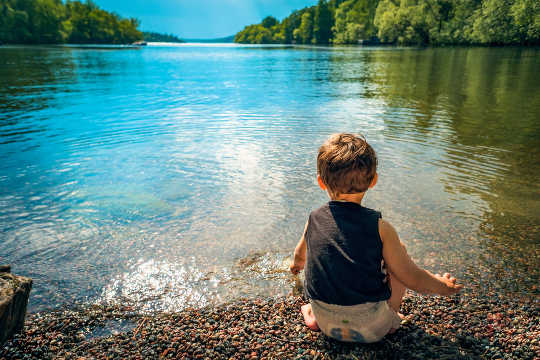 Attaining The Hidden Treasure of Infinite Joy and Happiness young child sitting at the edge of a peaceful lake