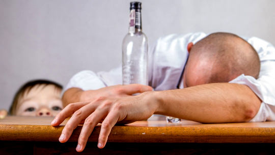 Can LSD Cure the 'Spiritual Disease' of Alcoholism? man passed out on a table with an empty bottle of alcohol with child looking on