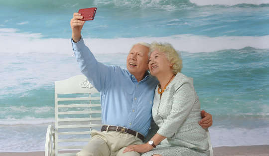 Marital Expectations According to Astrology older white-haired couple sitting on a bench at the beach taking a selfie