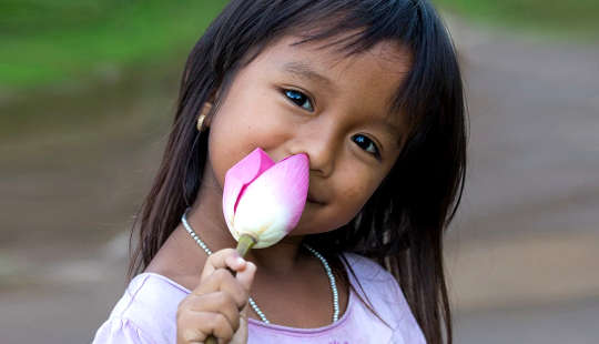The Lotus Within You Awakes smiling young girl holding an unopened lotus flower