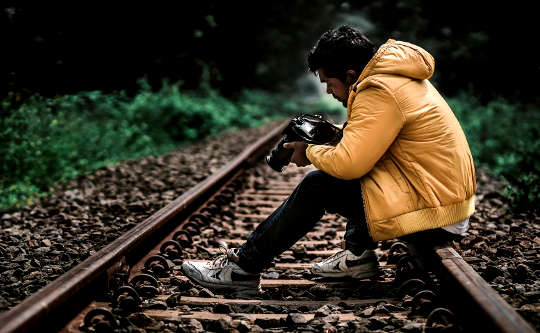 Don’t Be Afraid to Look More Deeply into Yourself young man sitting on the railroad tracks looking at the pictures in his camera