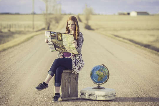Today's Inspiration: November 10, 2022 a young woman sitting on a suitcase in the middle of the road with a globe of planet earth next to her
