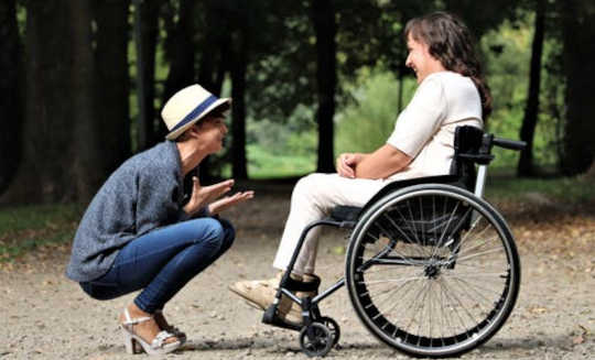 The Ups and Downs of Caregiving caring person squatting down in front of another in a wheelchair