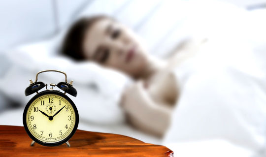 Time to Recharge: Optimizing Sleep Is Part of a Pain Solution a woman sleeping with an old-style non-electronic alarm clock on the nightstand