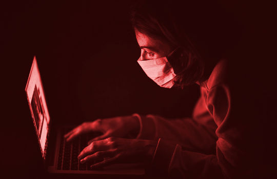 Coronaphobia: A New Epidemic of Isolation a person wearing a surgical mask working at a computer