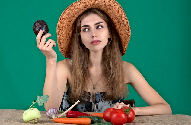 The Radical Act of Weaving Intuitive Eating and Intellect a woman with an array of fresh vegetables in front of her and holding up an avocado