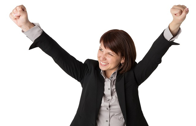 The Power of Humor in the Workplace: When and How to Embrace It woman with a huge smile, wearing a suit, and with her arms up in the air in victory